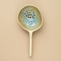 Stenen serveerlepel met gaatjes mosterd/blauw op warme beige achtergrond, studiofoto